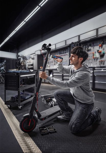 A person repairs an electric scooter using a cordless screwdriver in a workshop.
