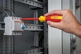 Person uses insulated screwdriver to adjust wiring in an electrical panel.
