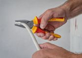 A person uses insulated pliers to grip and bend a thick white cable.