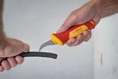 A person slices open a thick cable using an insulated safety knife.