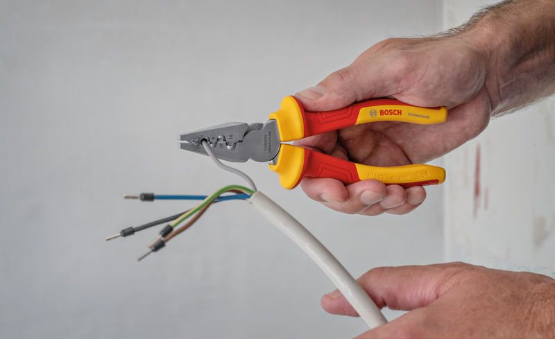 Person strips insulation from electrical wires using insulated pliers.