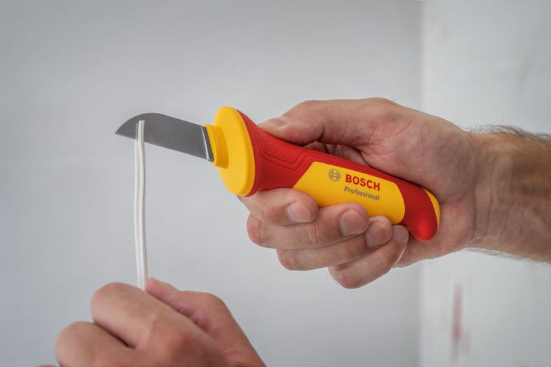 A person uses an insulated utility knife to cut electrical wiring.