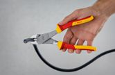 A person uses insulated diagonal side cutter pliers to cut a thick cable.