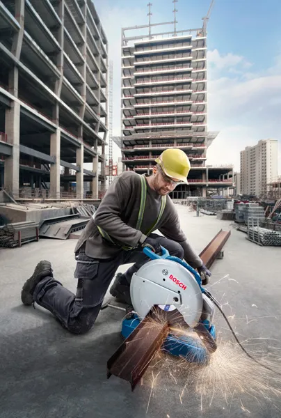 A person wearing safety equipment cuts a steel beam with a circular saw at a construction site.