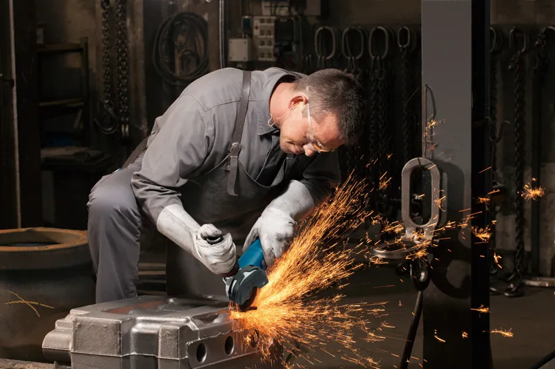 A person wearing safety equipment grinds a metal surface with an angle grinder.