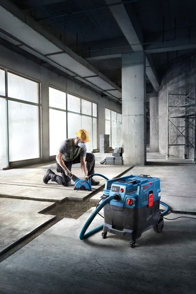 A person wearing safety equipment operates an all-purpose extractor on a concrete floor.
