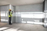 A person wearing safety equipment uses a laser leveling tool to project a straight line on a wall.