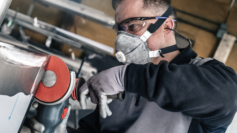 Person wearing safety equipment polishes metal with a power tool.