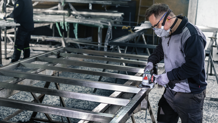 A person wearing safety equipment grinds a metal frame in a workshop.