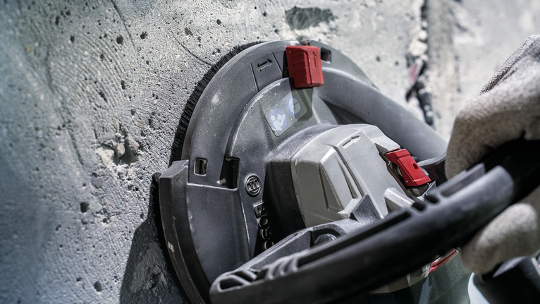 Person wearing safety equipment grinds a concrete wall with a power tool.