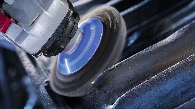 Rotary tool with a wire brush attachment cleans rust from a grooved metal surface.