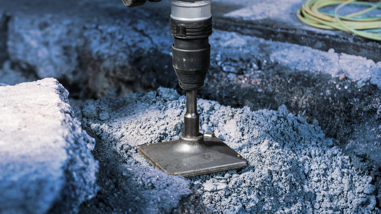 A power tool breaks through concrete with a flat chisel attachment.