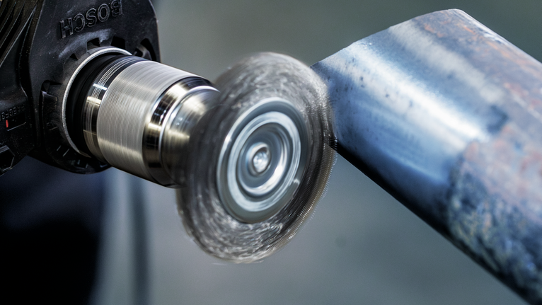 Rotary brush tool polishing a metal pipe surface.