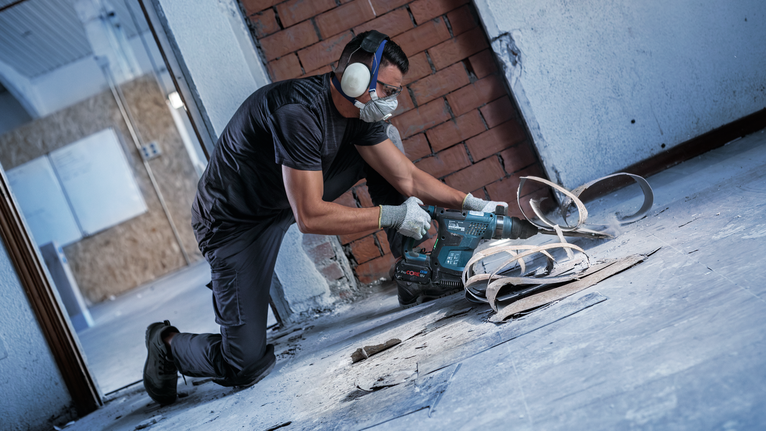 Person wearing safety equipment drills into a concrete floor during renovation.