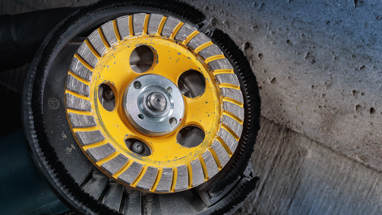 Diamond cup wheel grinder smoothing a rough concrete surface.