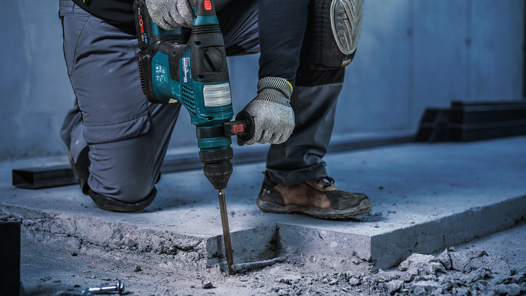 Person wearing safety equipment drills into a concrete floor with a rotary hammer.