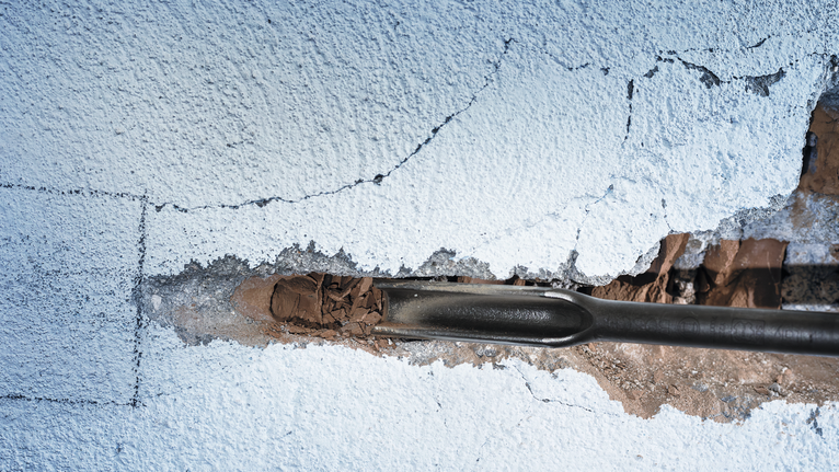Chisel tool breaking through plaster on a wall.
