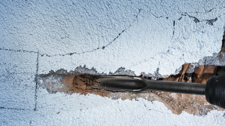 Chisel demolishing a cracked concrete wall.