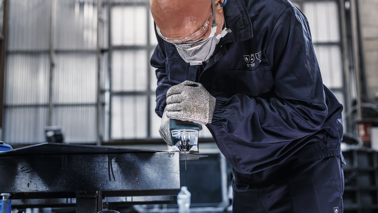 Person wearing safety equipment cuts metal using a handheld power saw.