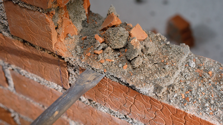 Chisel removing mortar and bricks from a damaged brick wall.