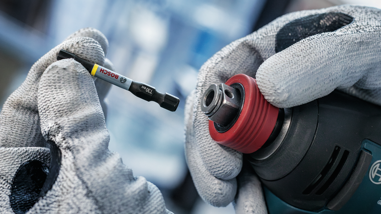 Person wearing safety equipment inserts a screwdriver bit into a power drill.