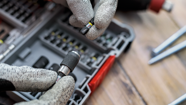 Person wearing safety equipment selects a screwdriver bit from an organized case.