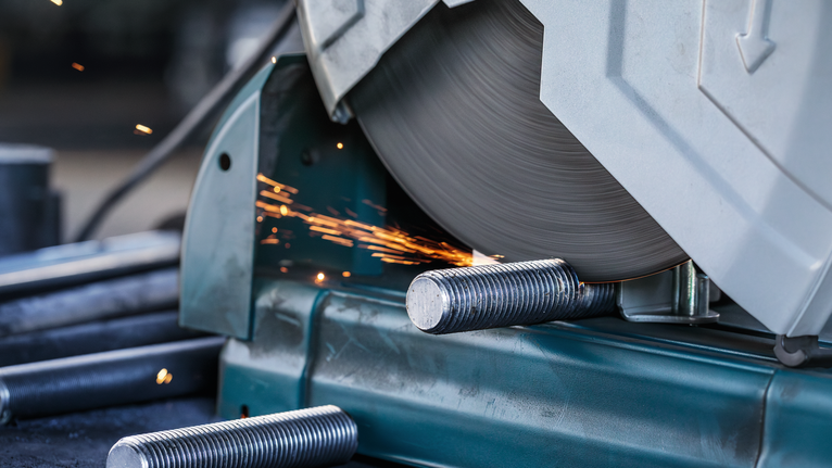Metal cutting saw slicing through steel rods, sending sparks flying.