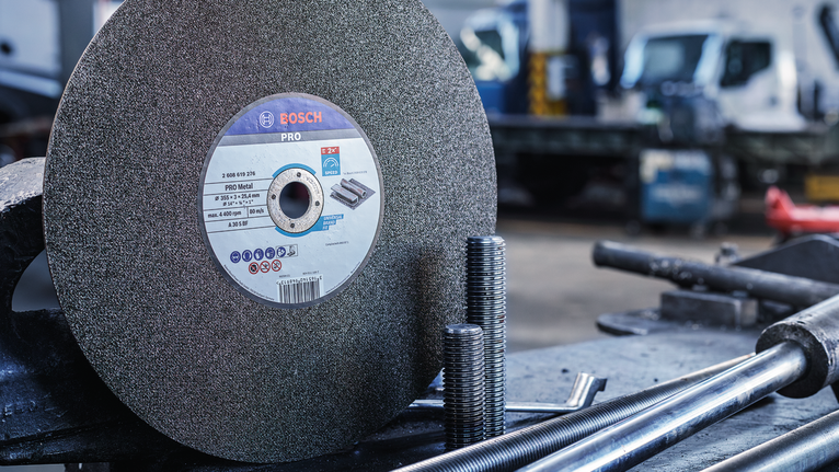 Large abrasive cutting wheel on a workbench beside threaded metal rods.