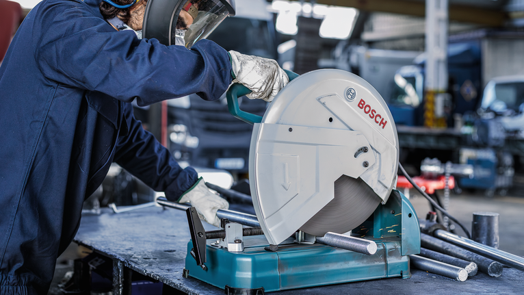 A person wearing safety equipment operates a circular saw to cut metal pipes.
