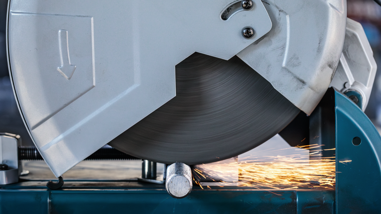Metal cutting saw slicing through a pipe with bright sparks flying.