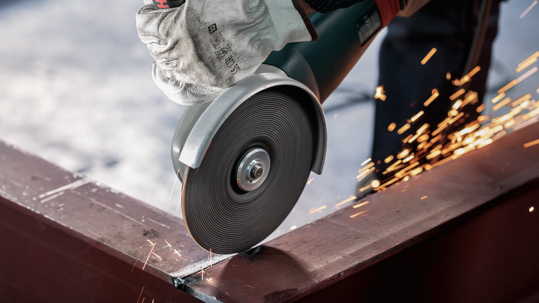 A person wearing safety equipment cuts metal with an angle grinder, producing sparks.