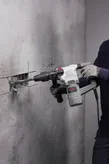A person wearing safety equipment uses a rotary hammer to chisel a groove in a concrete wall.