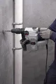 A person wearing safety equipment drills into a concrete wall with a rotary hammer.