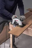 A person wearing safety equipment uses a circular saw to cut wooden flooring.
