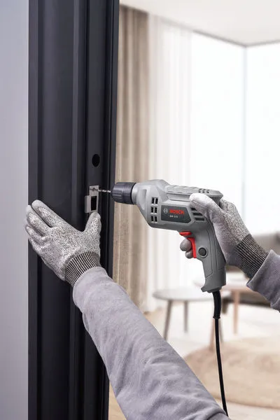 A person wearing safety equipment drills into a metal door frame.
