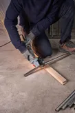 A person wearing safety equipment cuts a metal pipe with a grinder on a concrete floor.