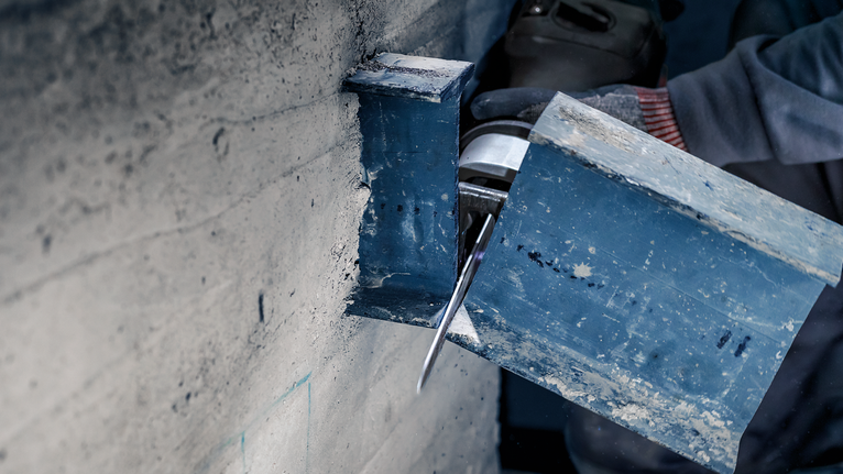 Person wearing safety equipment cuts a steel beam with a power tool.