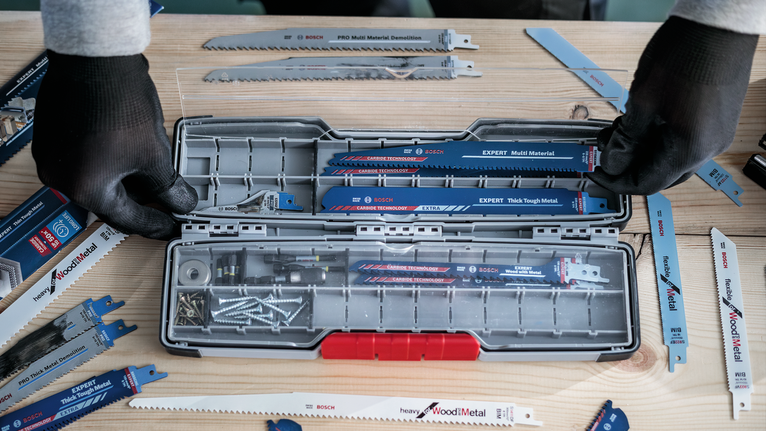 Person wearing safety equipment organizes assorted saw blades and screws in a tool case.