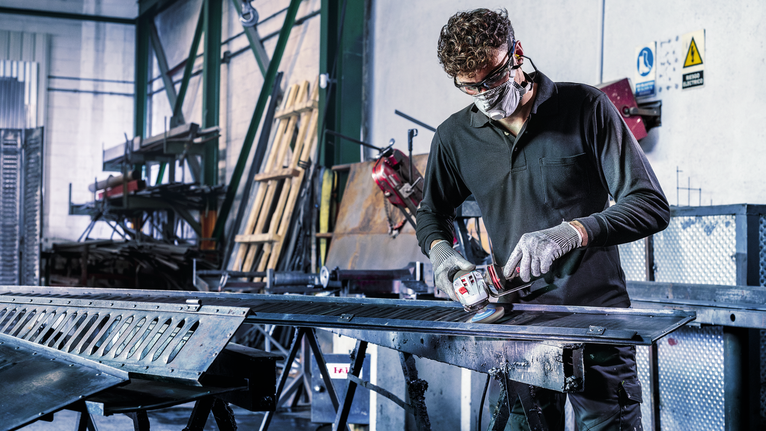 A person wearing safety equipment grinds metal in an industrial workshop.