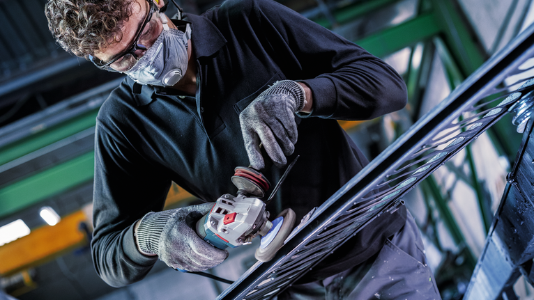 Person wearing safety equipment grinds metal rail with an angle grinder.