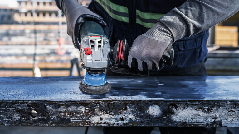 Person wearing safety equipment polishes a metal surface with an angle grinder.