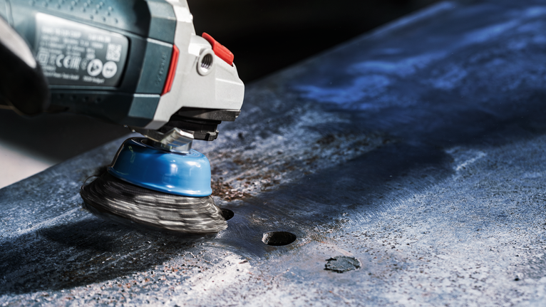 Wire cup brush grinder smoothing a metal surface.
