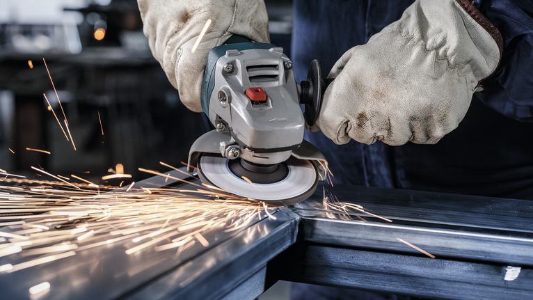 Person wearing safety equipment grinds metal, producing bright sparks.