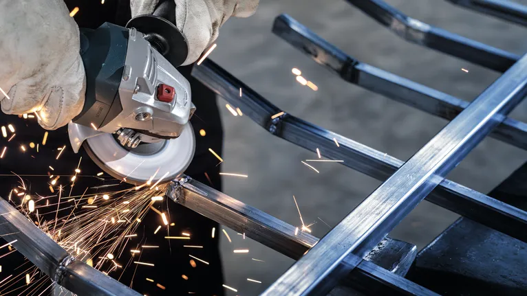 Person wearing safety equipment grinds a metal frame, creating sparks.