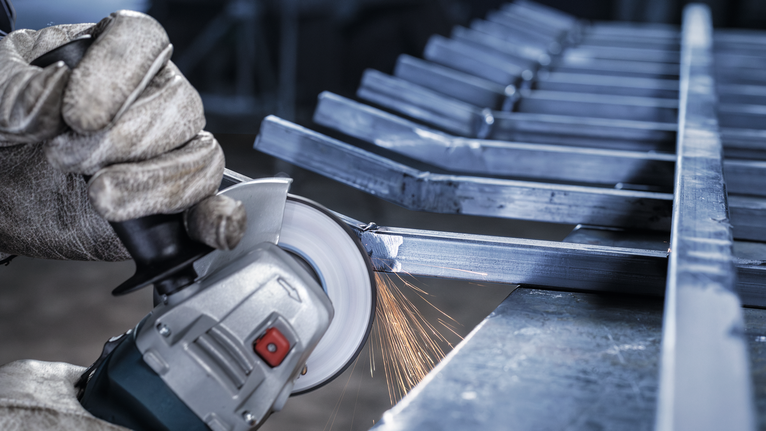 Person wearing safety equipment grinds metal bars with an angle grinder, creating sparks.