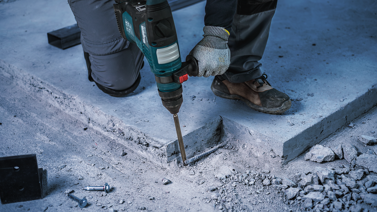 Person wearing safety equipment uses a power tool to break concrete.