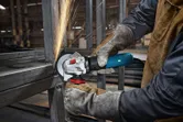 A person wearing safety equipment grinds metal, creating sparks in an industrial setting.