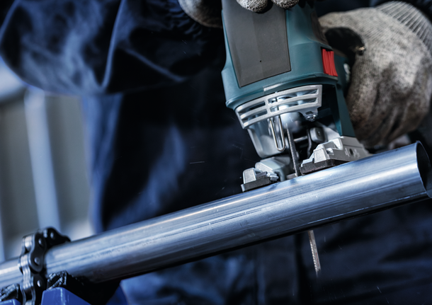 Person wearing safety equipment uses a jigsaw to cut a metal pipe.