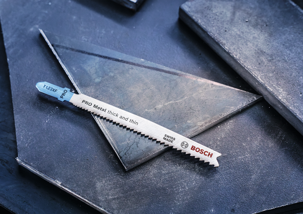 Metal jigsaw blade resting on dark metal sheets.