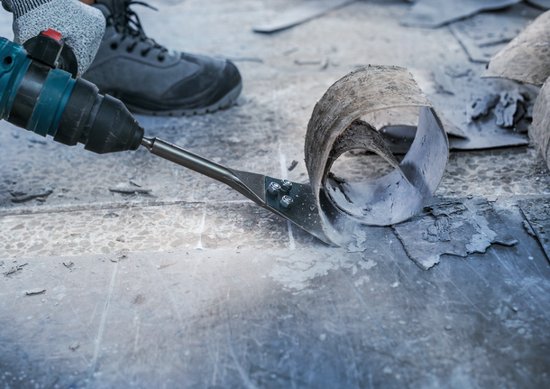 Person wearing safety equipment uses a power tool to remove flooring material.